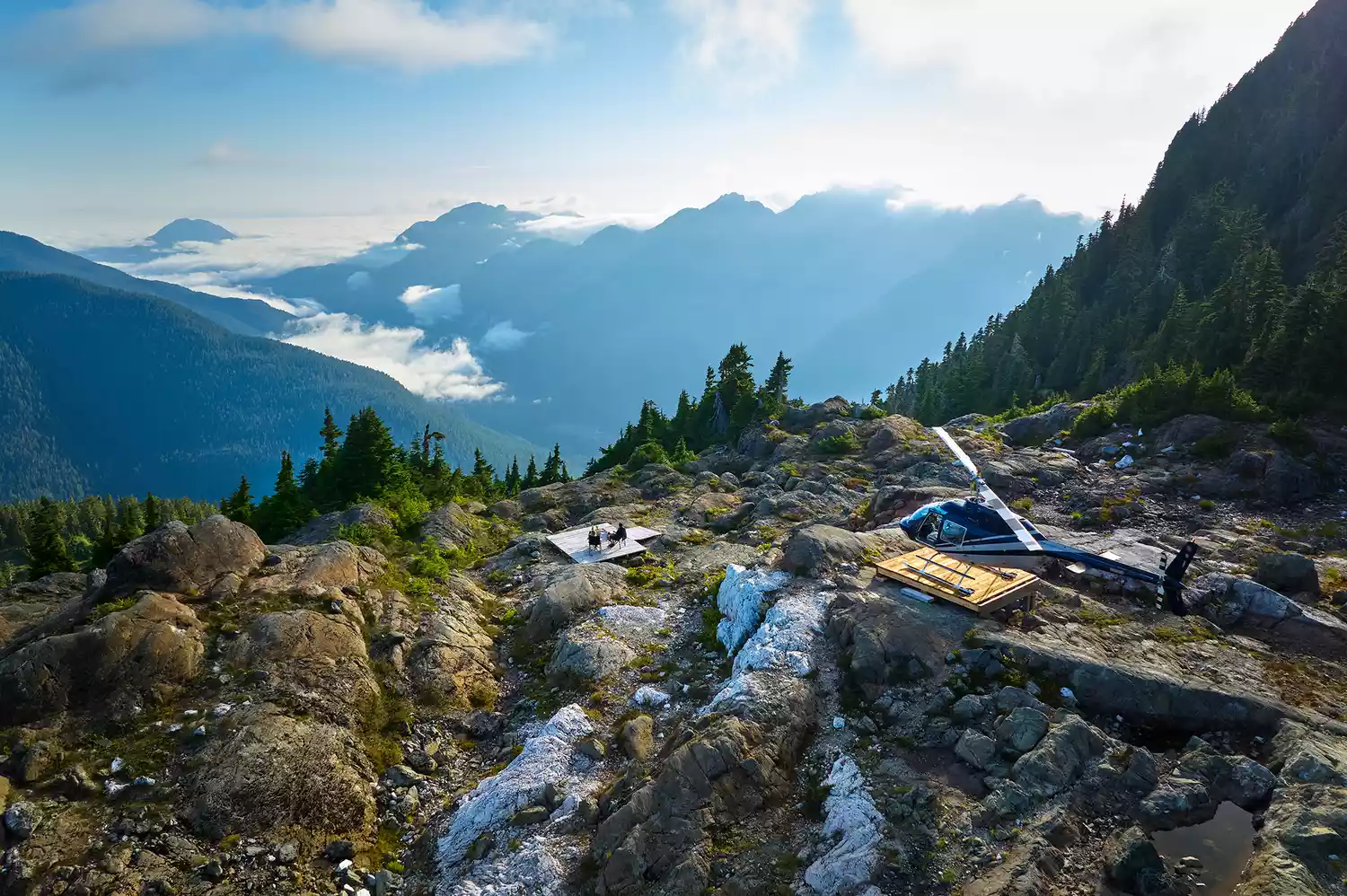 A white helicopter parked on a mountain ridge overlooking the fjords of Vancouver Island.