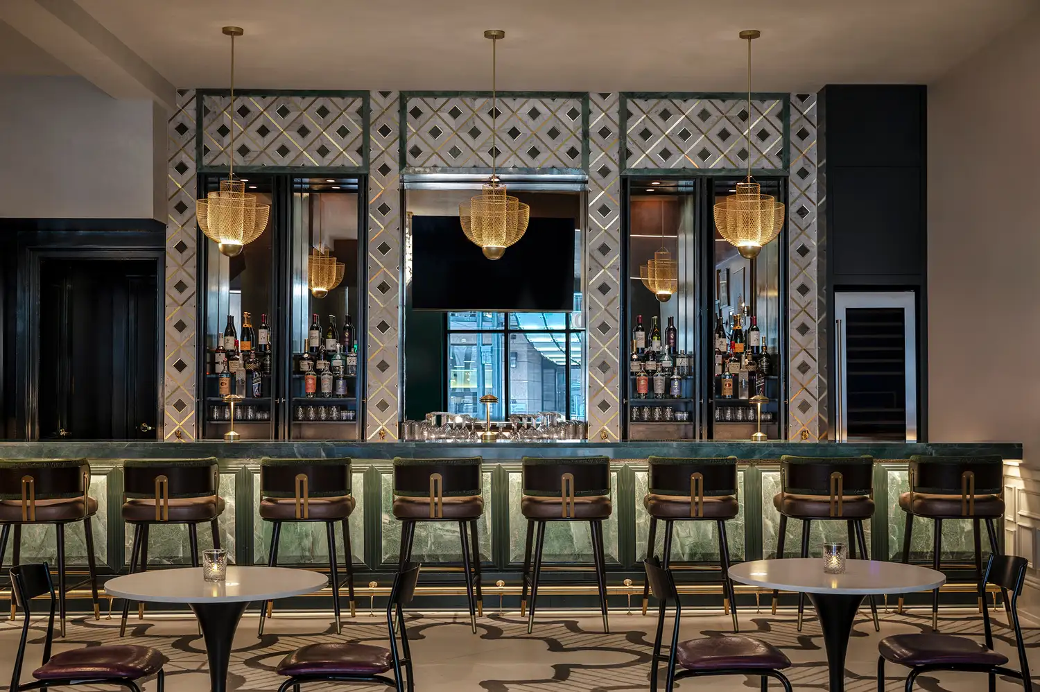 A modern bar with stools, hanging lights, and bottles displayed on shelves at The Monarch.