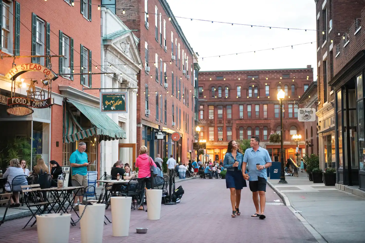 Pedestrians walking and dining on Linden Street under string lights in downtown Geneva NY.