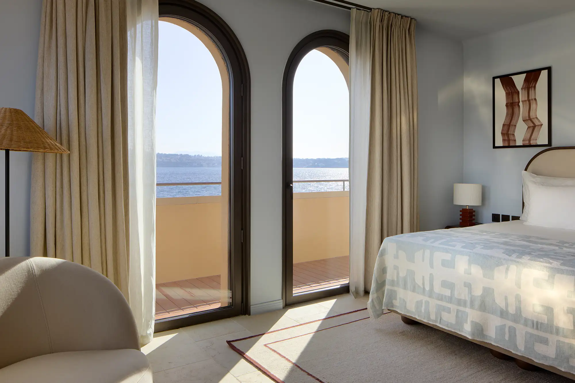 Sunlit luxury bedroom with elegant arched windows opening to a private balcony and ocean view.