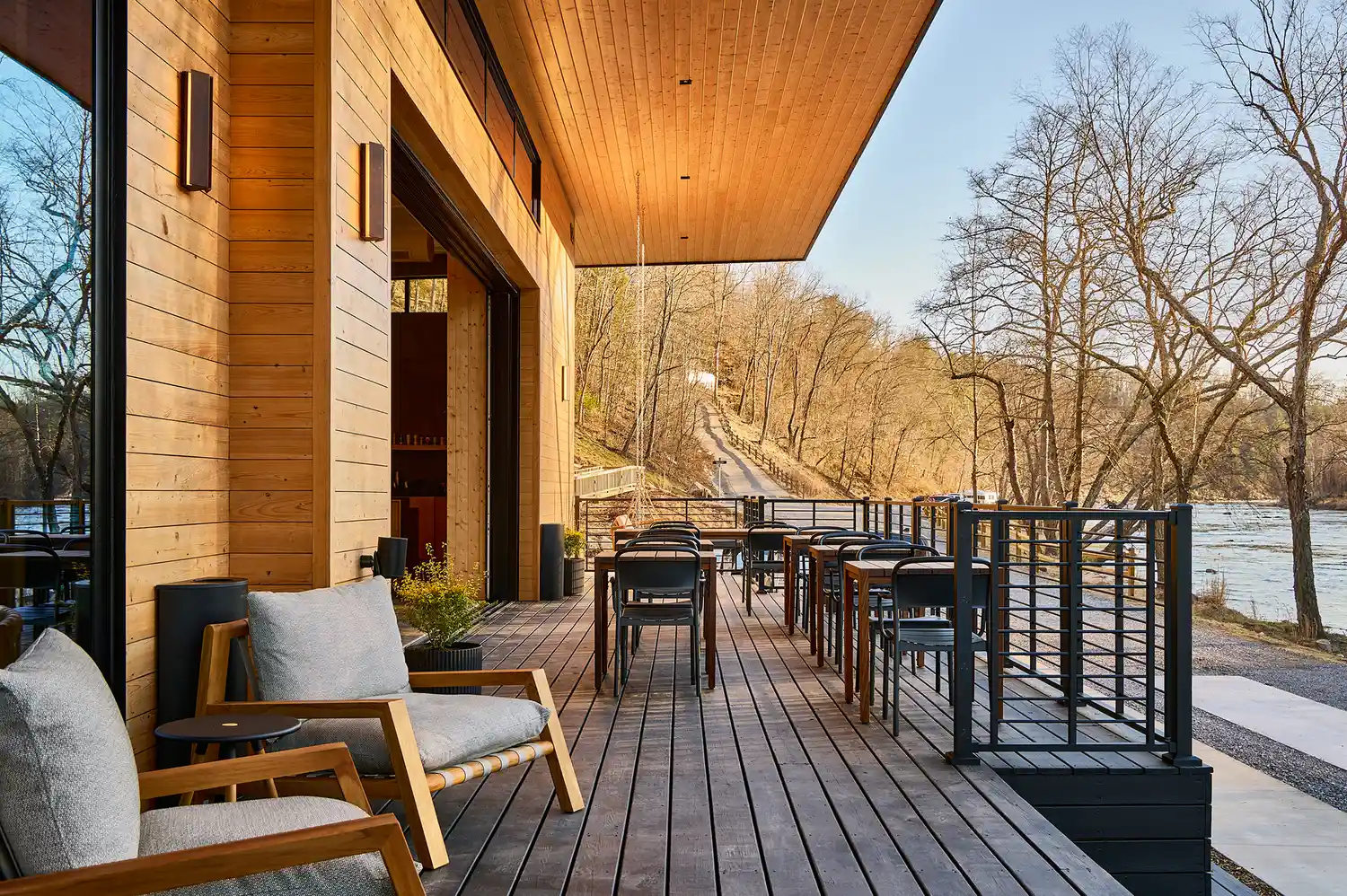 An outdoor wooden patio with seating area overlooking natural greenery near the French Broad River.