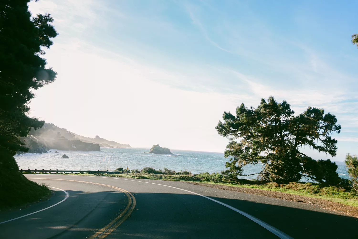 A winding section of the Pacific Coast Highway curving along the edge of steep coastal bluffs overlooking the ocean.