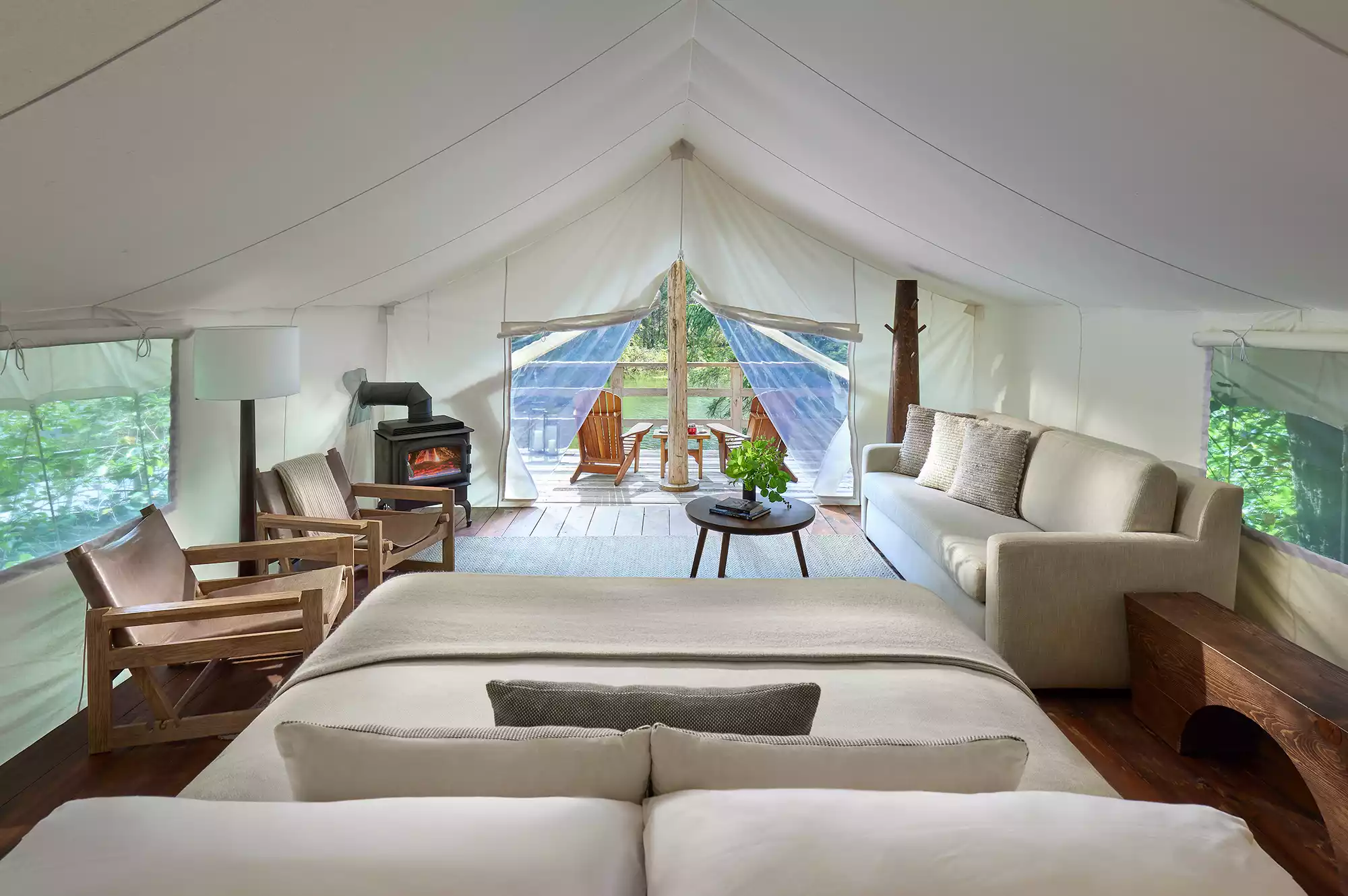 A large canvas prospector-style tent on a raised wooden platform surrounded by lush greenery.