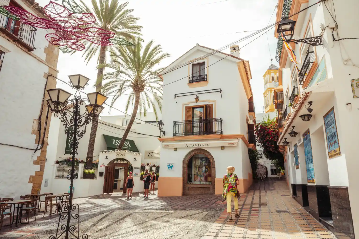 A bustling plaza in the Old Town with tourists walking near a historic church spire.