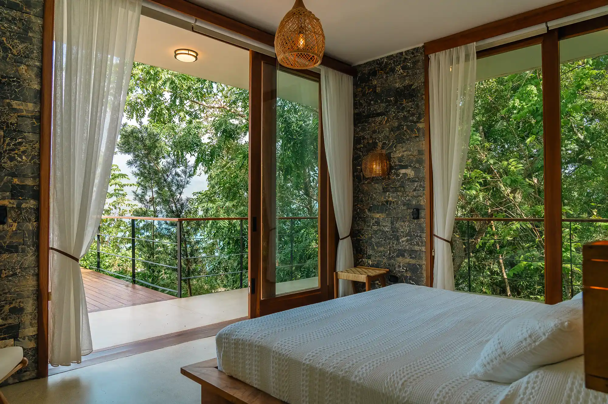Modern villa bedroom with expansive glass walls opening onto a balcony overlooking the rainforest.