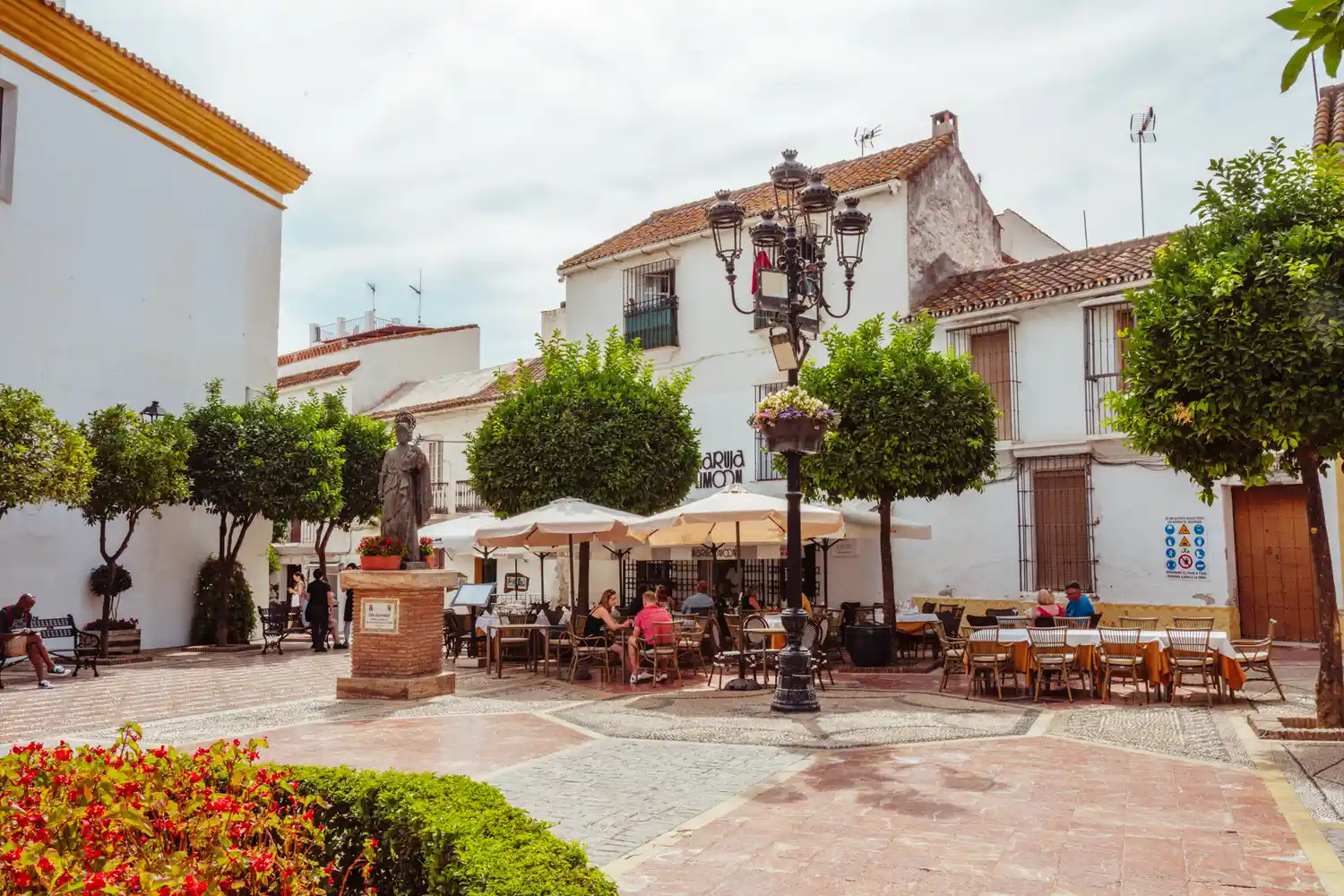 People enjoying sunny weather at outdoor cafe tables in a Marbella plaza.
