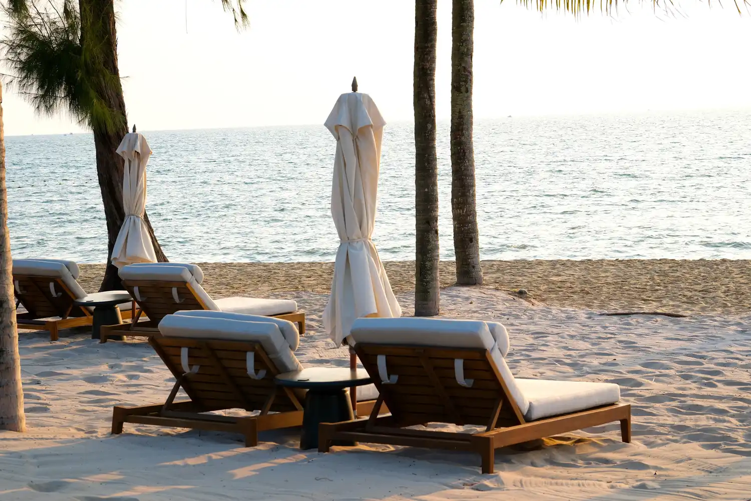 Two empty lounge chairs and umbrellas on a serene tropical beach.