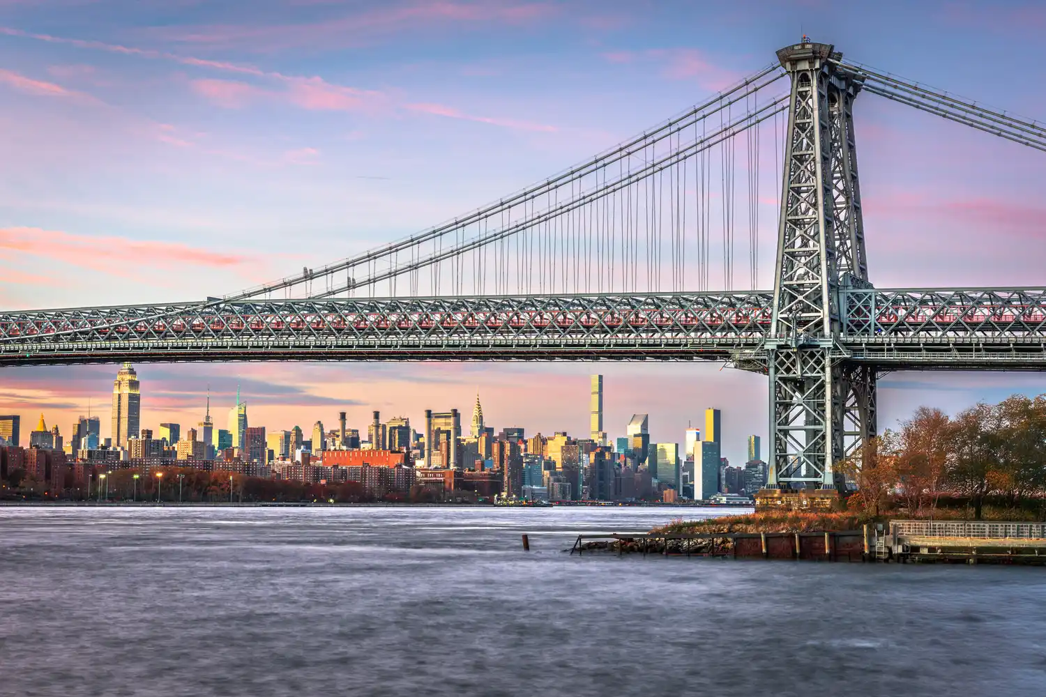 The Williamsburg Bridge with the New York City skyline in the background during the day.