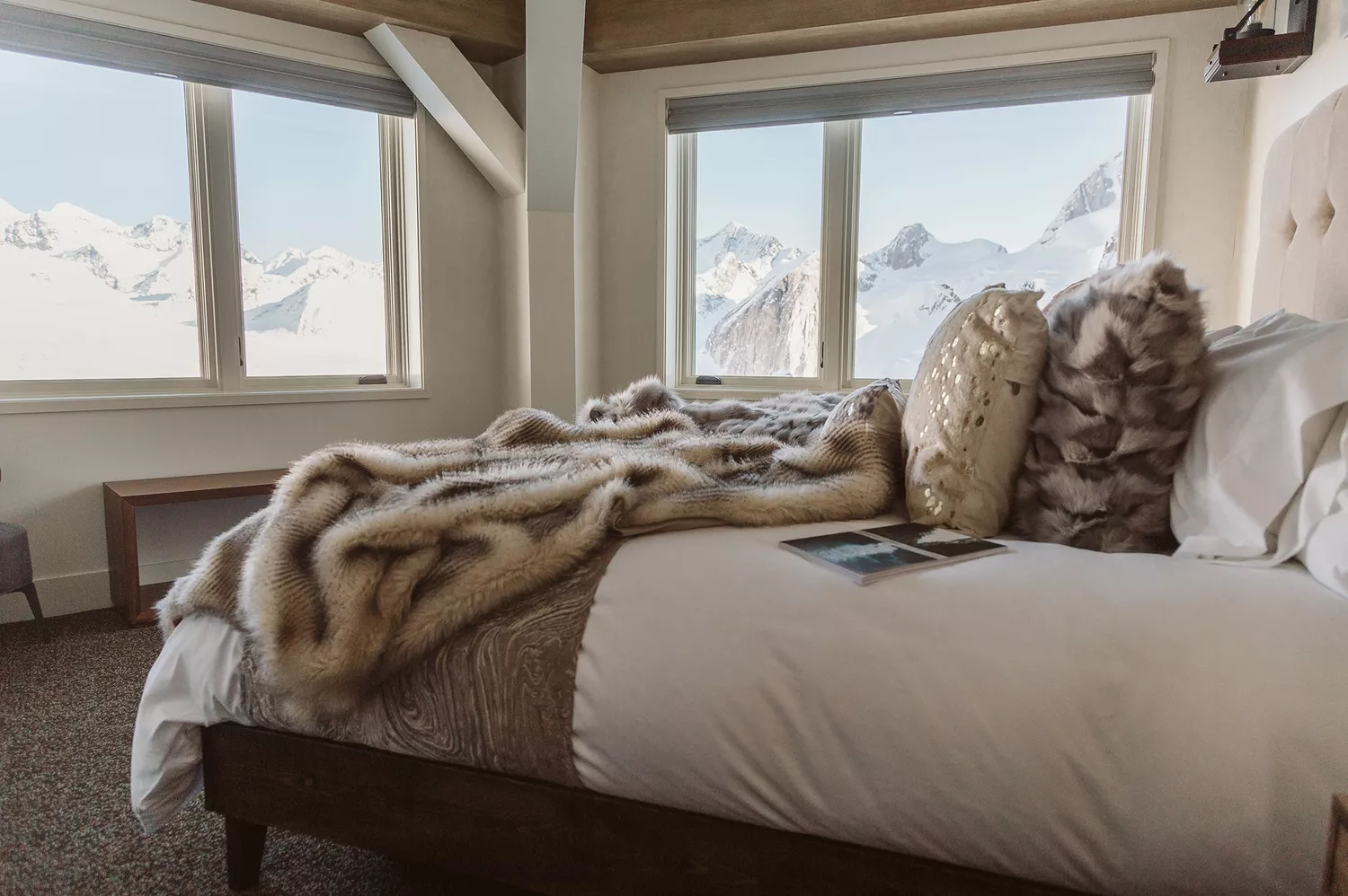 A luxury suite interior featuring warm wood finishes and a large panoramic window framing the Alaska Range peaks.