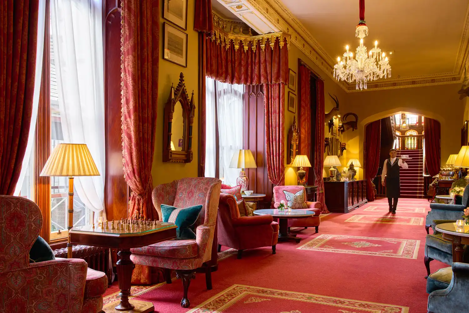 The long, opulent gallery hall inside Dromoland Castle with red carpets and classical furniture.
