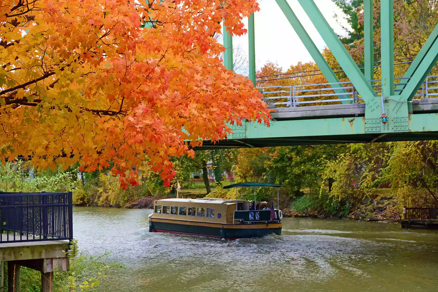 A narrow canal boat cruising through the Erie Canal surrounded by vibrant autumn foliage.