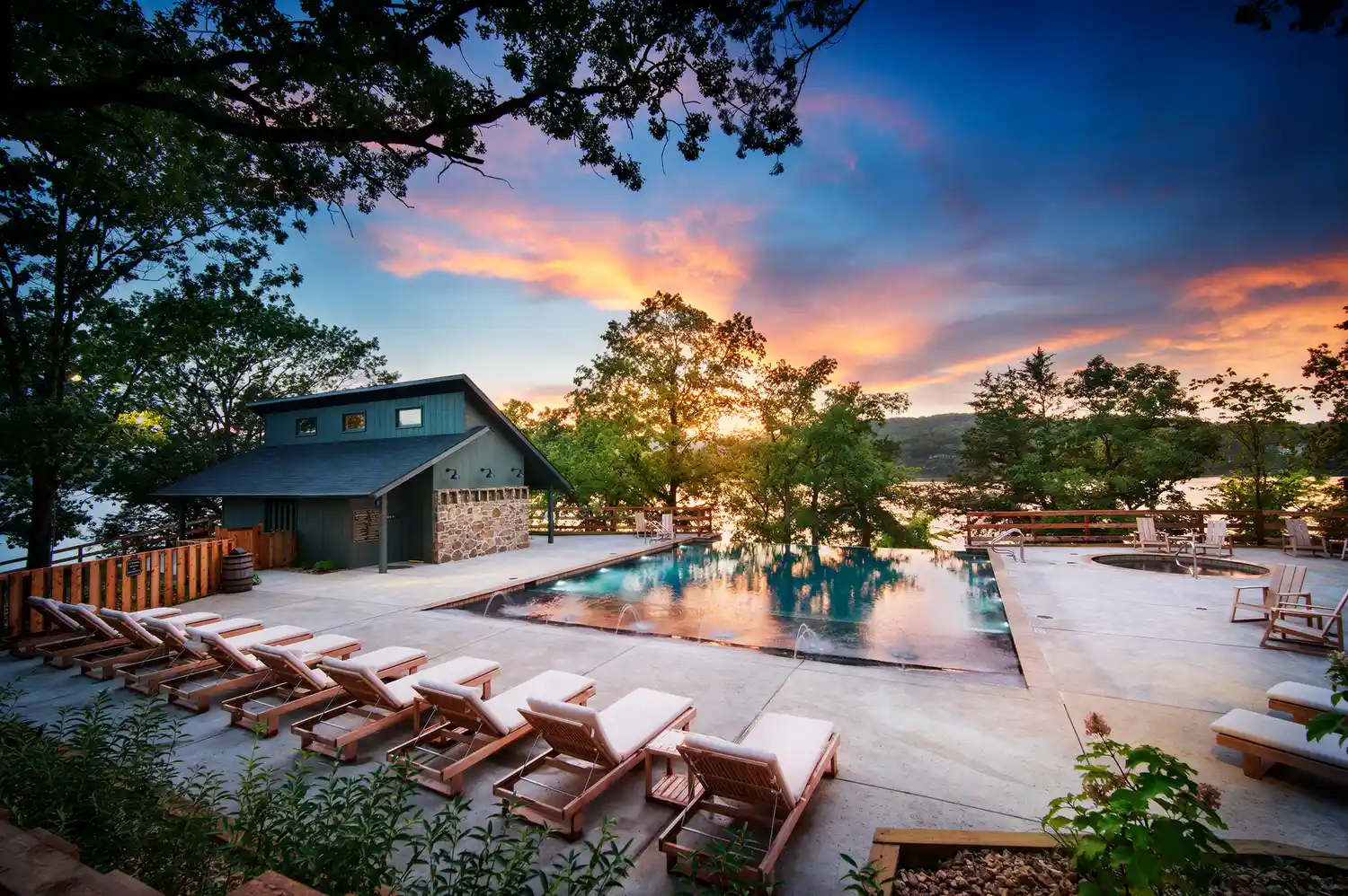 An outdoor infinity-style pool at sunset with empty lounge chairs overlooking the Ozarks.