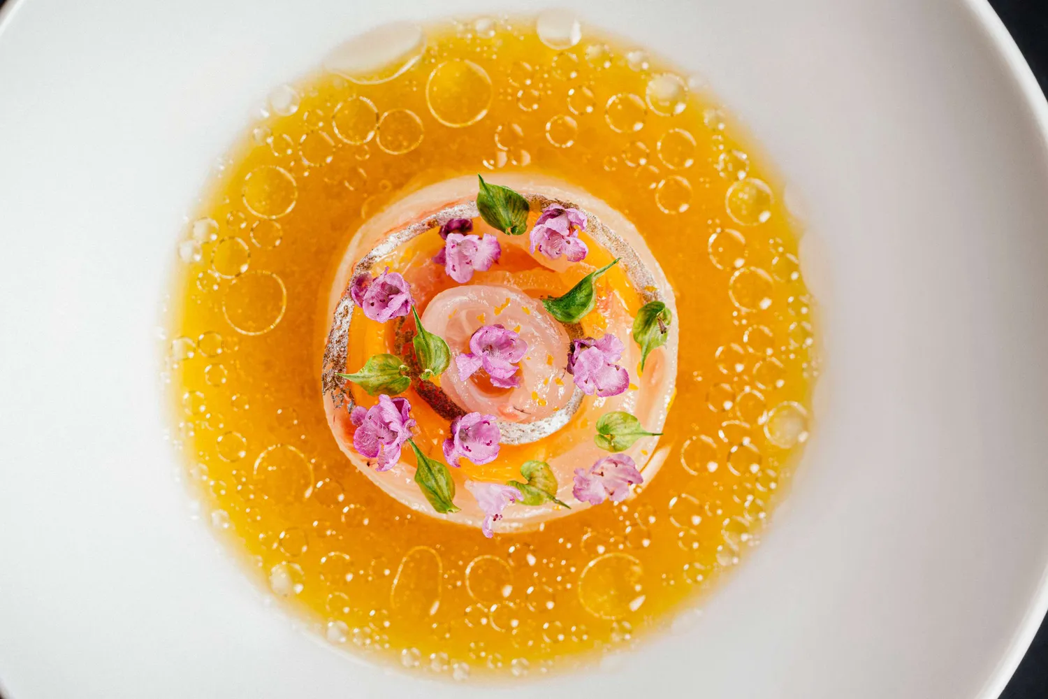 An elegantly plated gourmet dish with yellow sauce and edible flower garnishes.