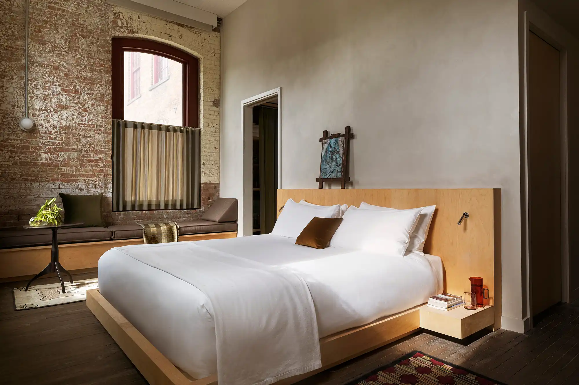 An industrial-chic guest room at Pocketbook Hudson featuring exposed brick and minimalist furniture.