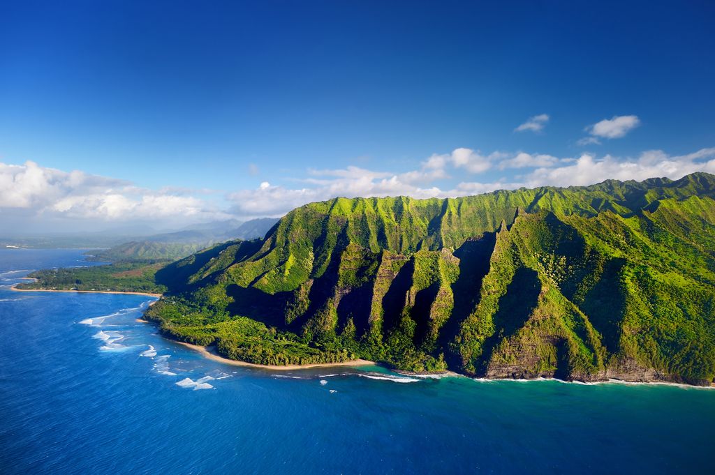 Aerial view of steep emerald green ridges and deep valleys along the Nā Pali Coast in Hawaii.