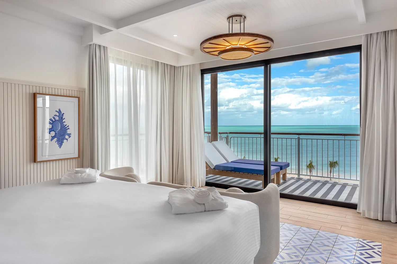 Modern hotel suite interior with a view of the ocean through large glass balcony doors.
