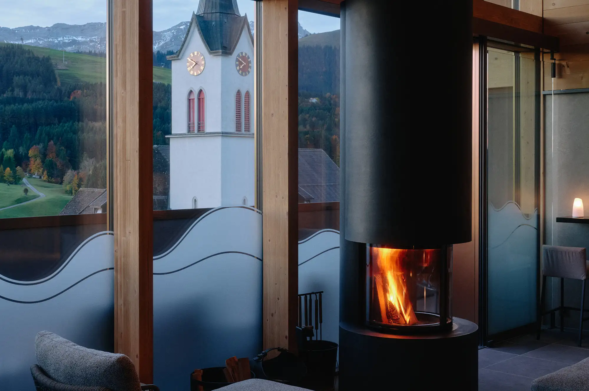 Cozy rooftop lounge with a modern fireplace and a view of a traditional Swiss church through the window.
