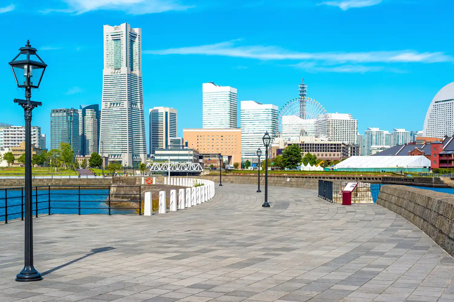 The Yokohama skyline featuring modern skyscrapers and the Ferris wheel on a sunny day seen from the water.