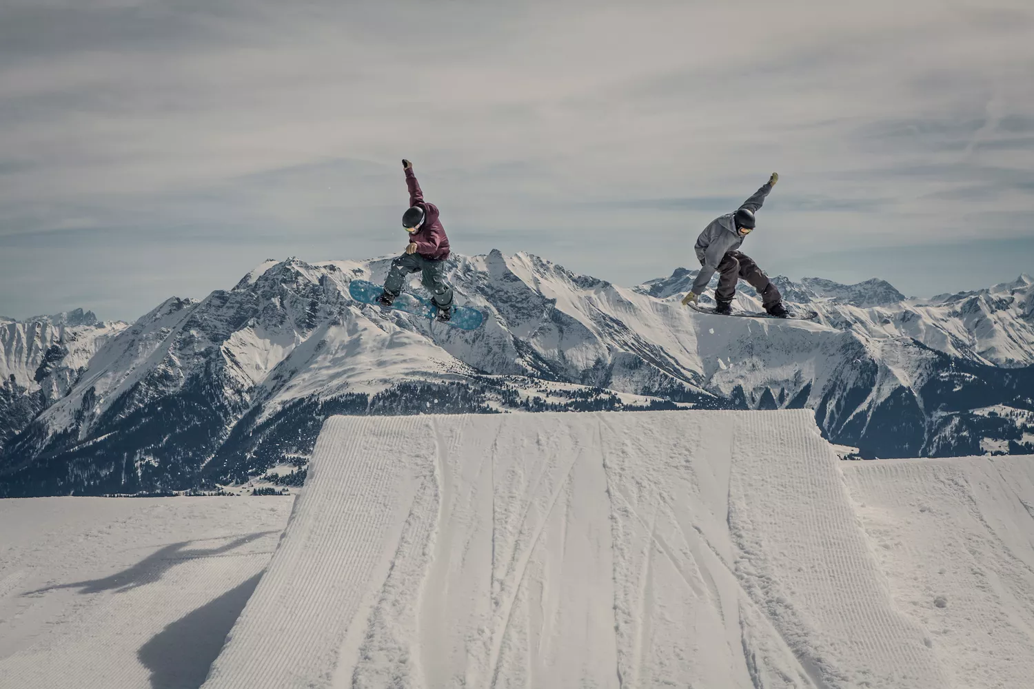 Two snowboarders performing a synchronized jump against a clear blue sky in Laax, Switzerland.