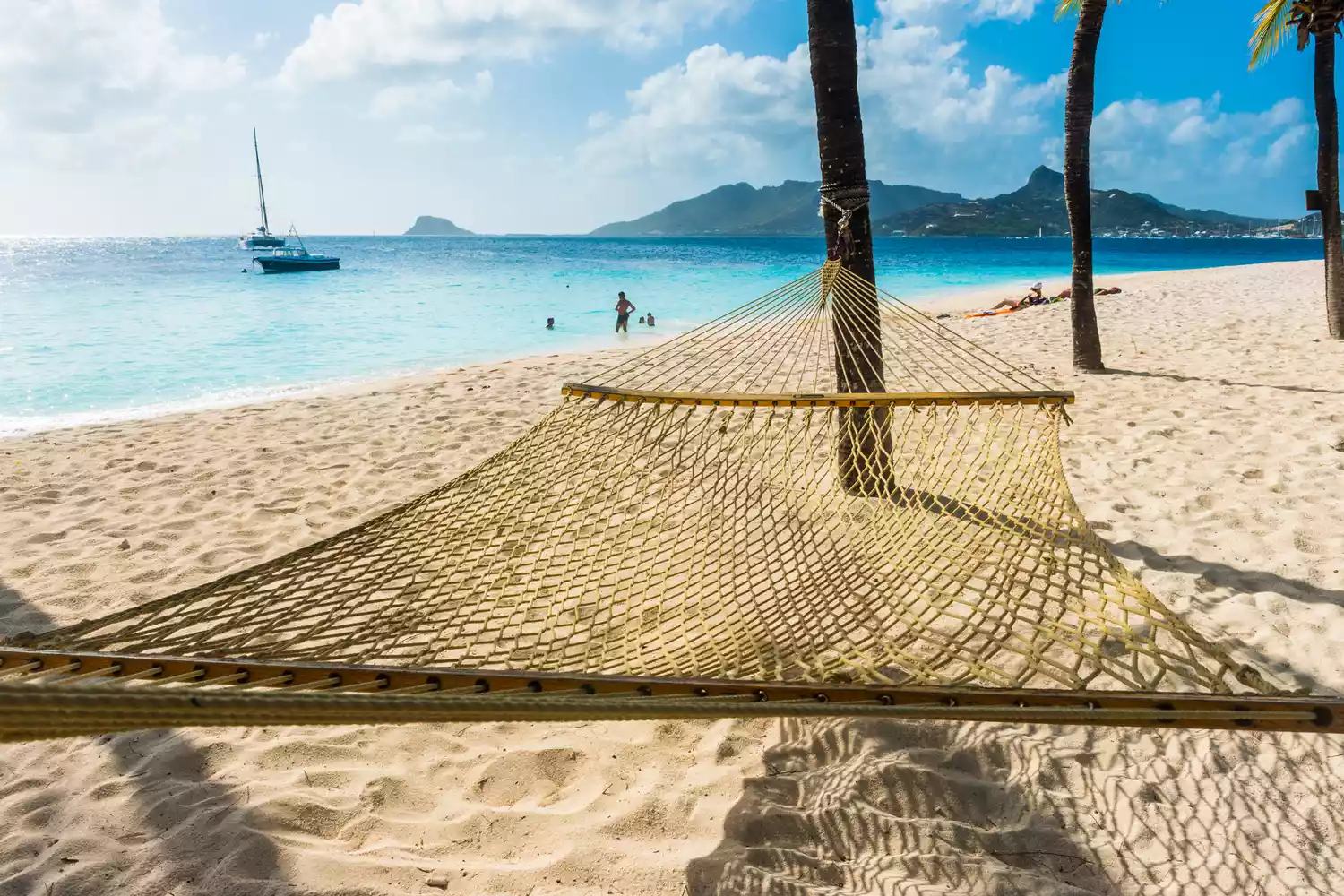 A white hammock hanging between palm trees on a pristine sandy beach in St. Vincent.
