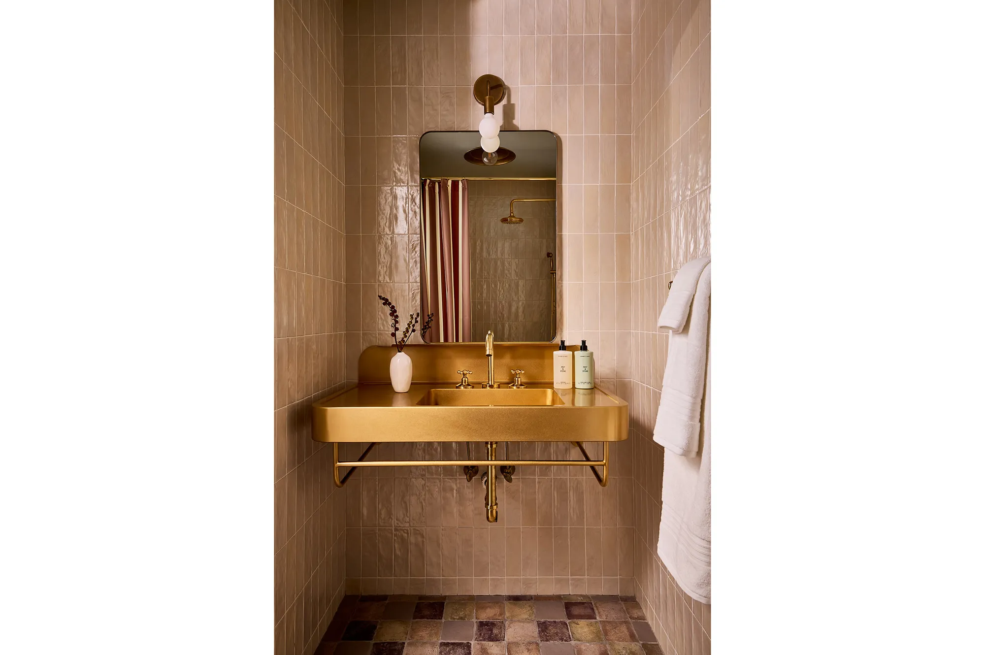 Luxury hotel bathroom featuring a gold-finished sink, circular mirror, and modern white tiling.