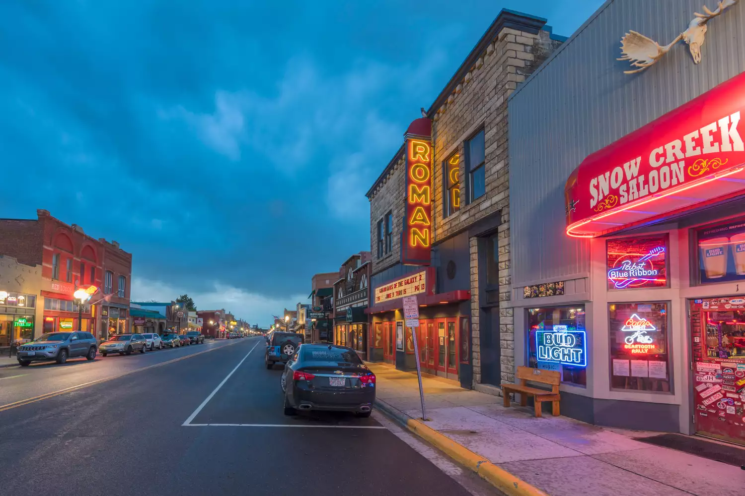The Snow Creek Saloon and other bars on Broadway Avenue at twilight with snow on the ground.