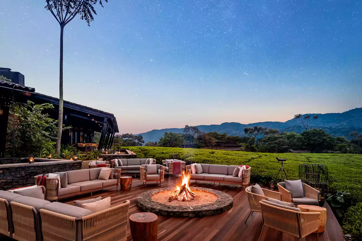 A fire pit glowing at twilight on a wooden deck at One&Only Nyungwe House surrounded by dense forest.