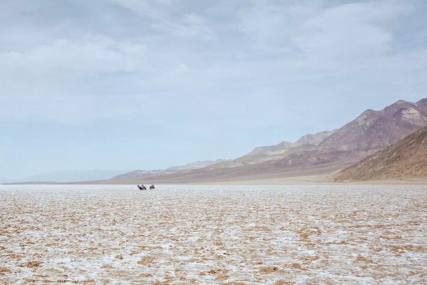 A group of people walking across the white salt flats of Death Valley under a bright sun.