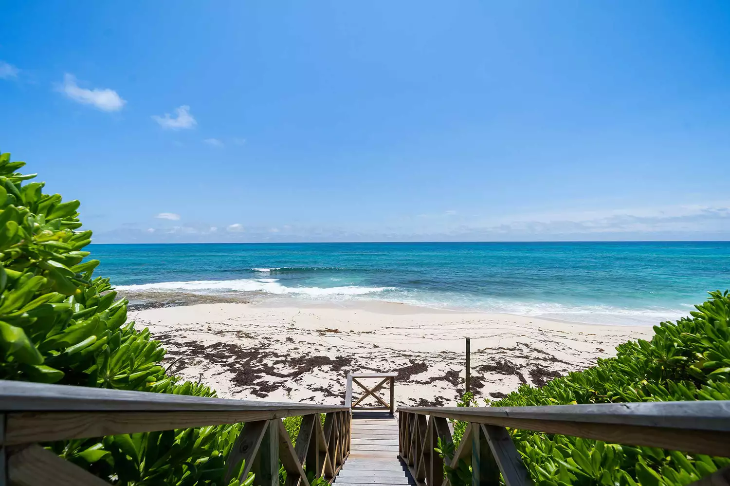 A sandy path leading through tropical vegetation to a white sand beach.