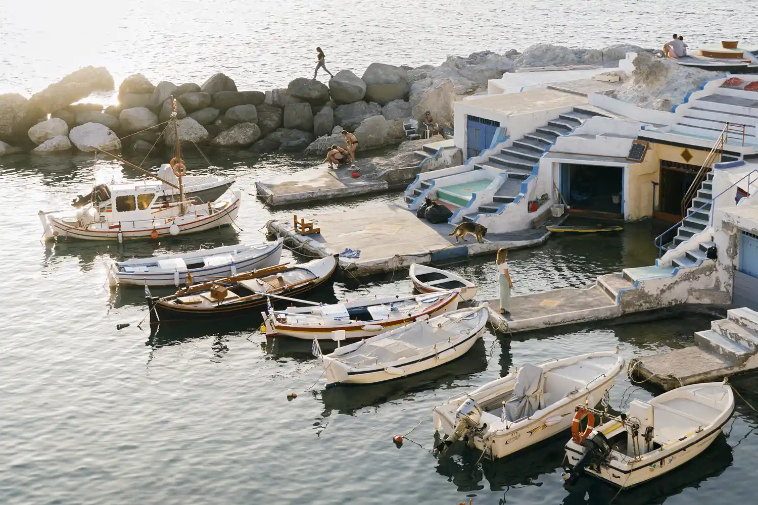 Traditional colorful fishing boats moored alongside white stone buildings in Milos.