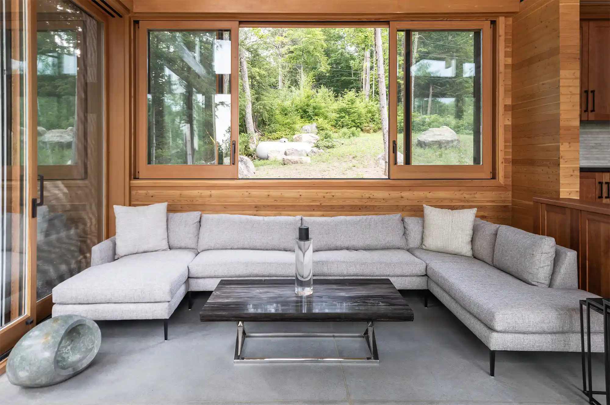 Living room with a sectional sofa and floor-to-ceiling windows looking out onto a lush forest.