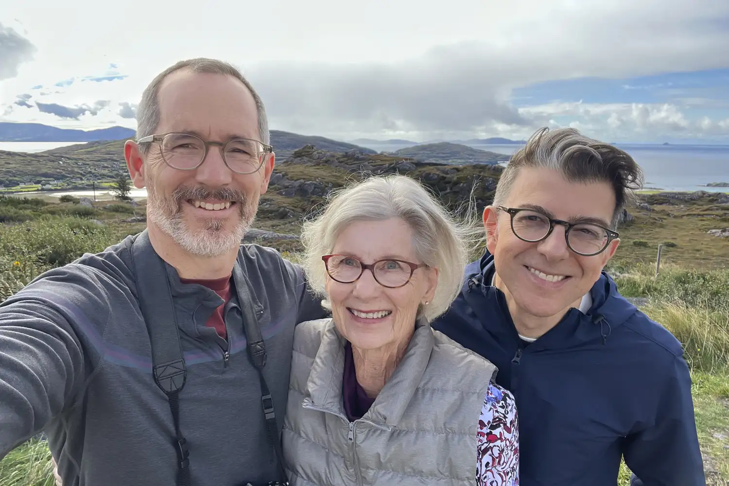 A multi-generational family of three smiling for a selfie in the Irish highlands.