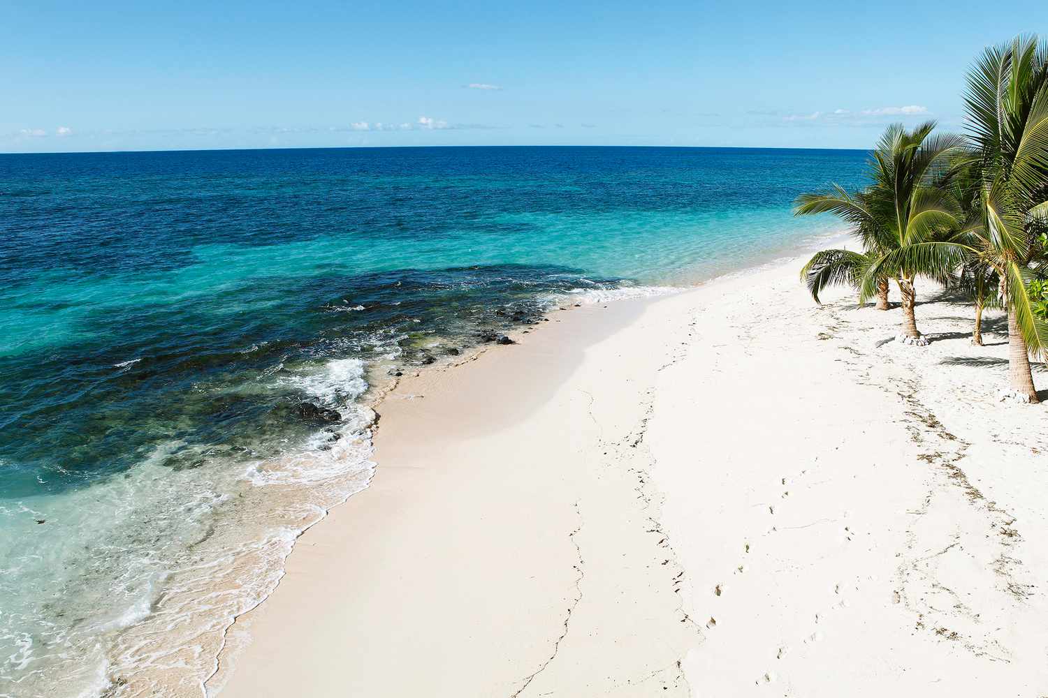 A pristine white sand beach in the Fiji islands with clear shallow water and palm trees.