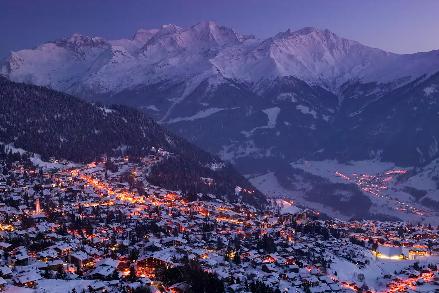 The village of Verbier illuminated at dusk with traditional Alpine architecture.