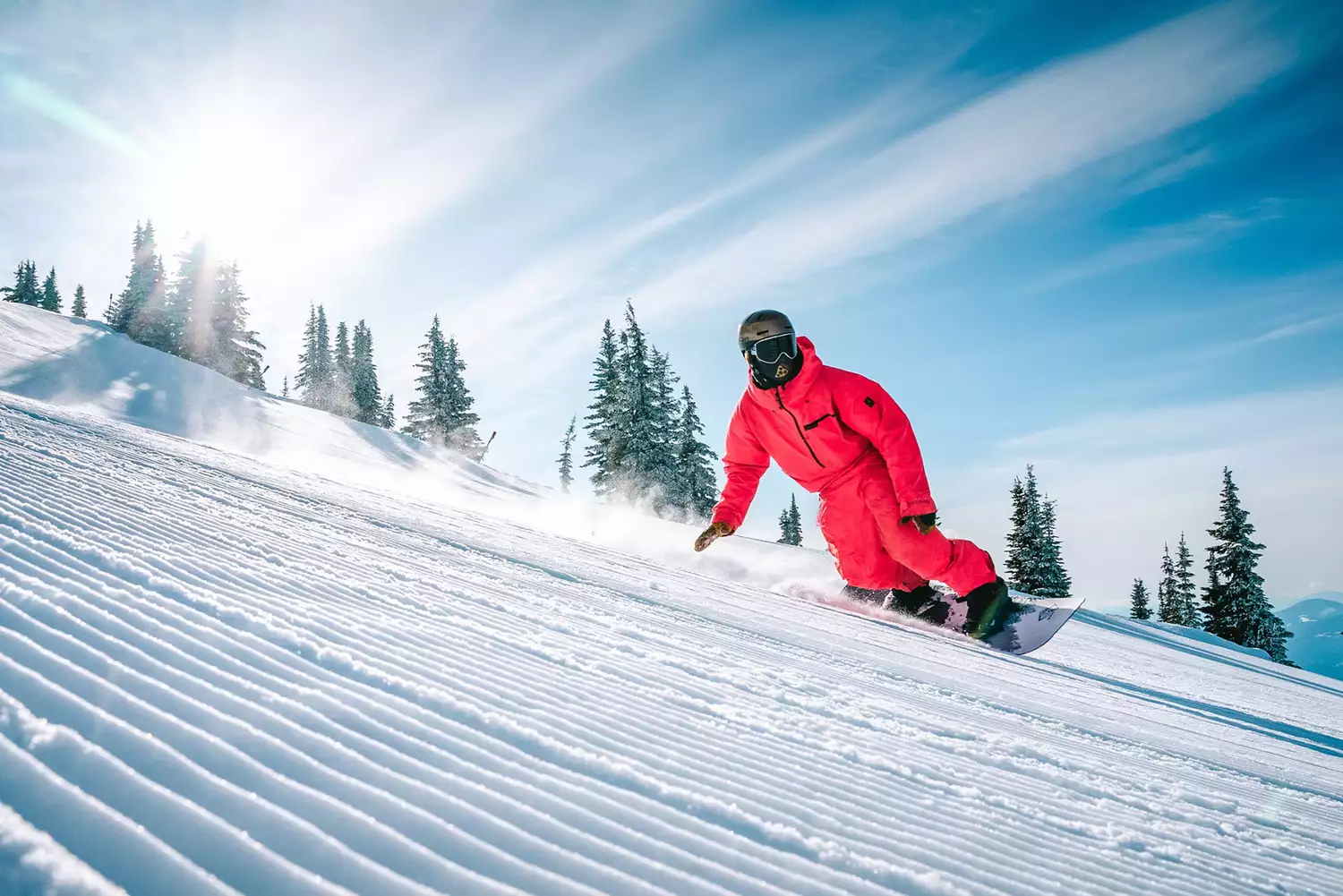 A snowboarder riding through deep powder snow among trees at Revelstoke Mountain Resort.