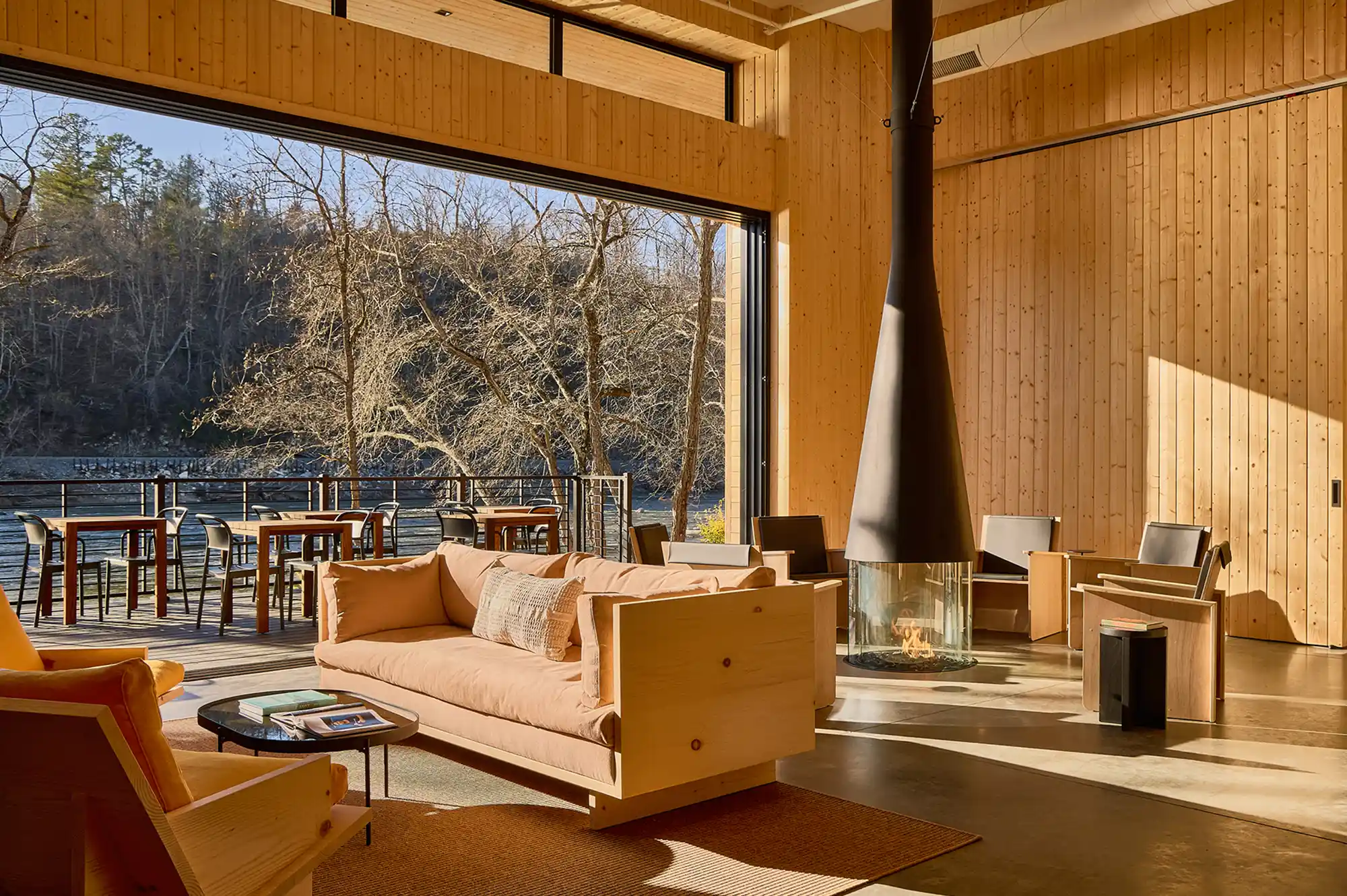Interior of a modern lounge with large glass windows overlooking a wooden deck and forest.