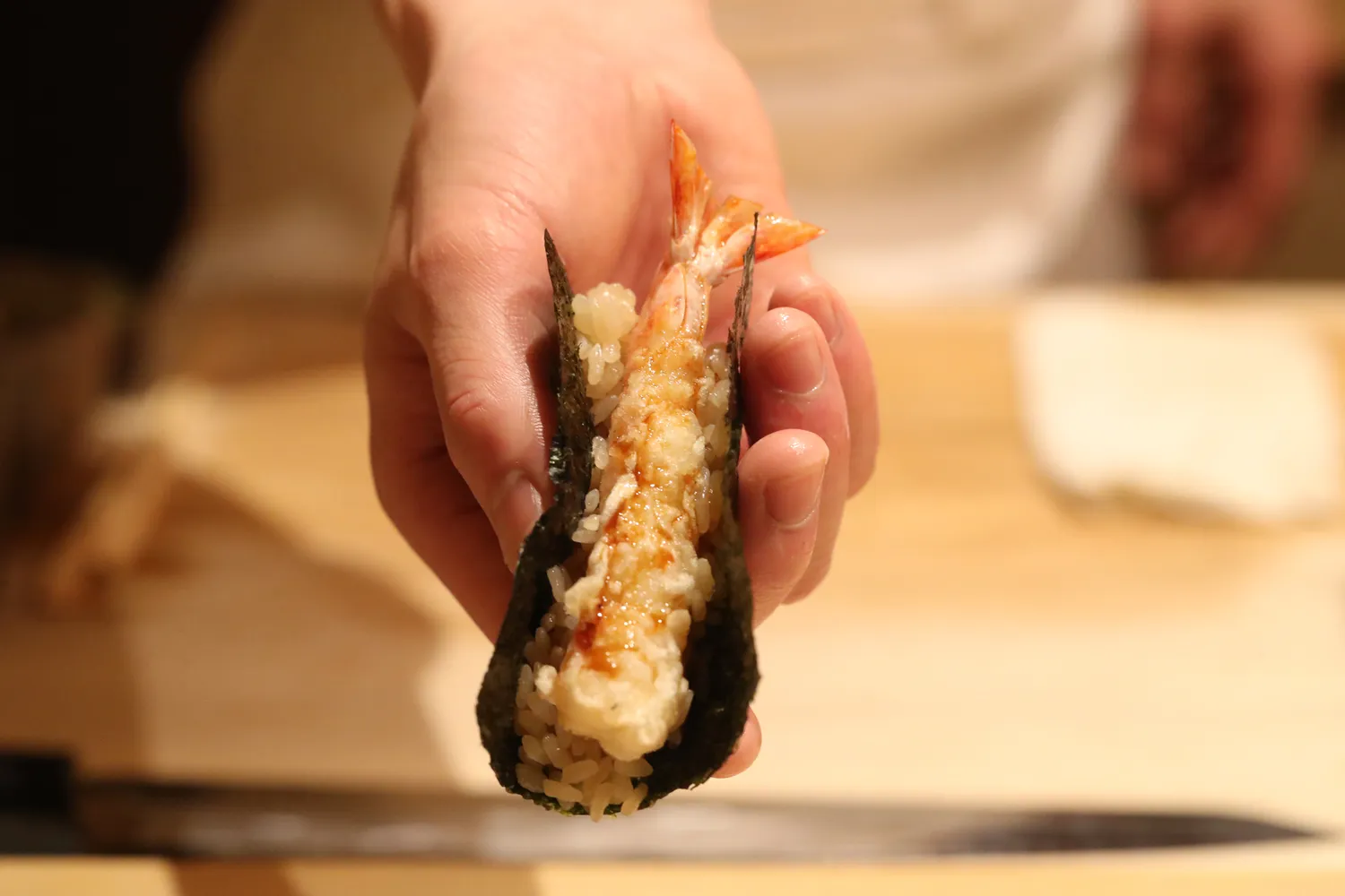 A close-up of a hand holding a piece of freshly prepared shrimp tempura.
