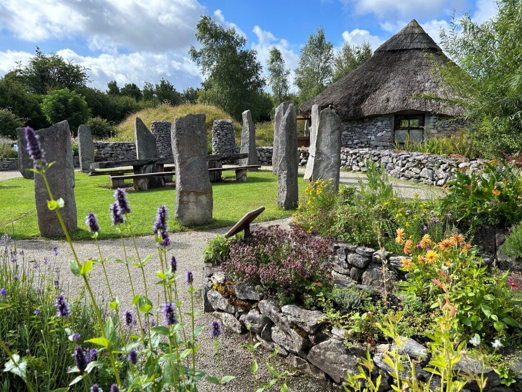 Ancient stone structures and grave markers in a grassy Irish landscape under a soft sky.