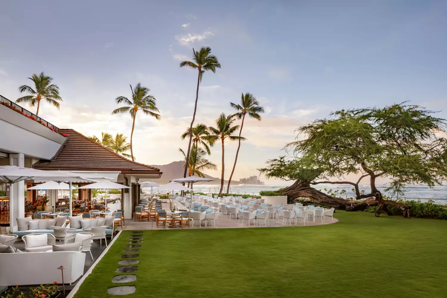 An outdoor patio restaurant at Halekulani with white linens set against a tropical backdrop.