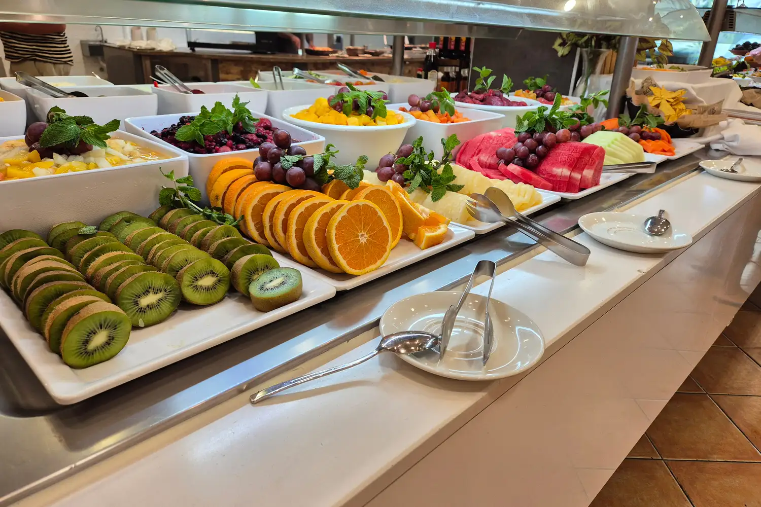 A variety of sliced fresh fruits including watermelon, kiwi, and grapes at a breakfast buffet.