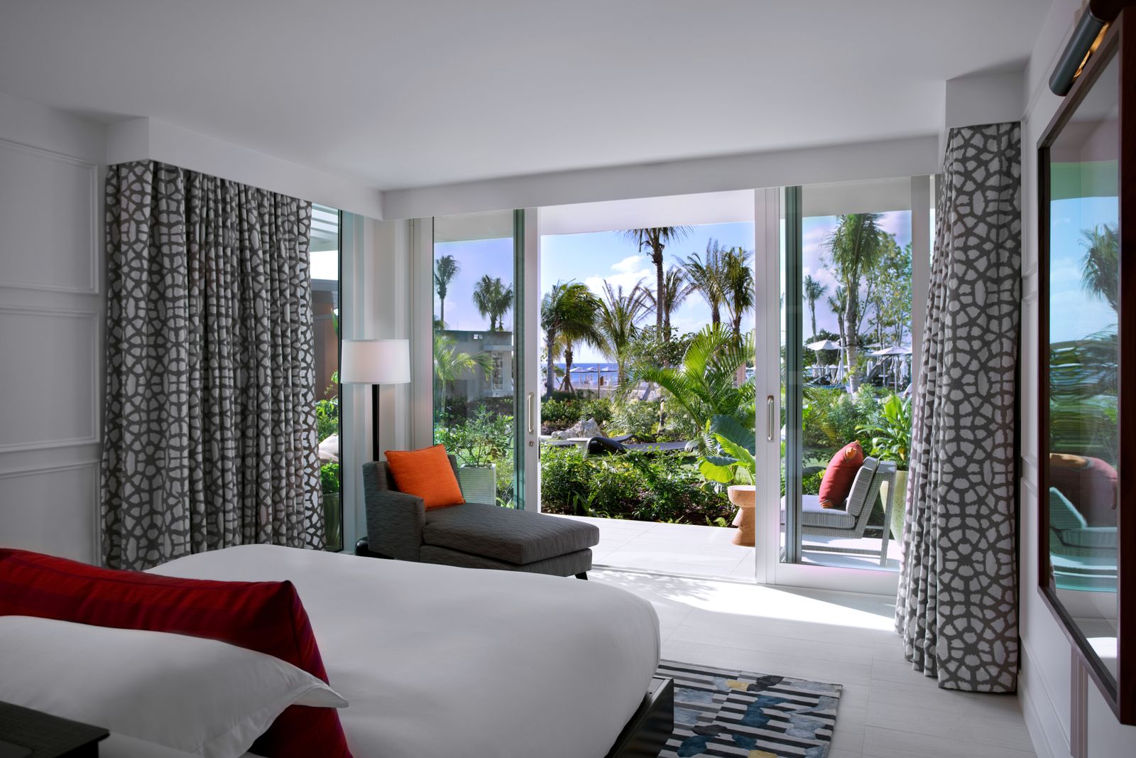 An elegant hotel suite interior with large windows looking out onto a tropical view.