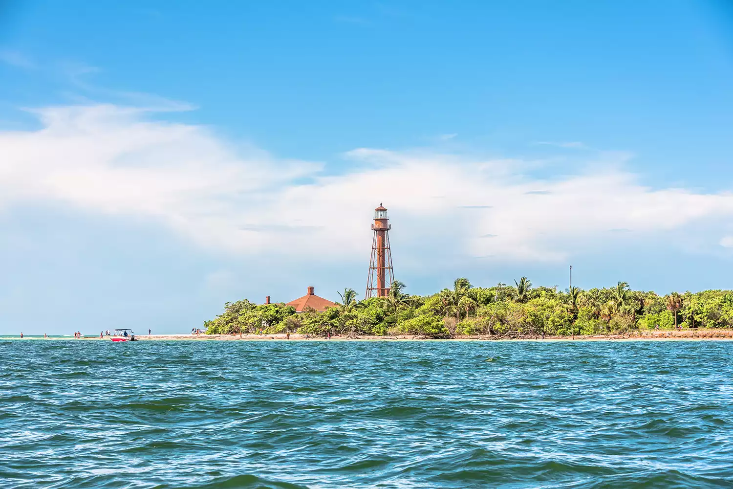 The historic Sanibel Island Lighthouse standing tall against a blue sky near the beach.