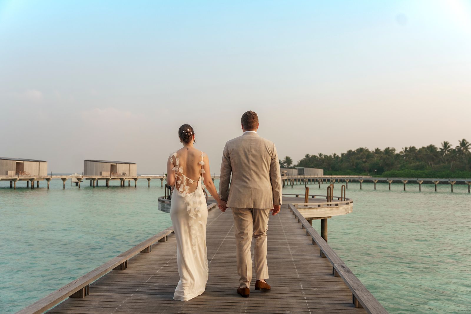 A close-up of a couple holding hands while standing by the edge of clear blue water.