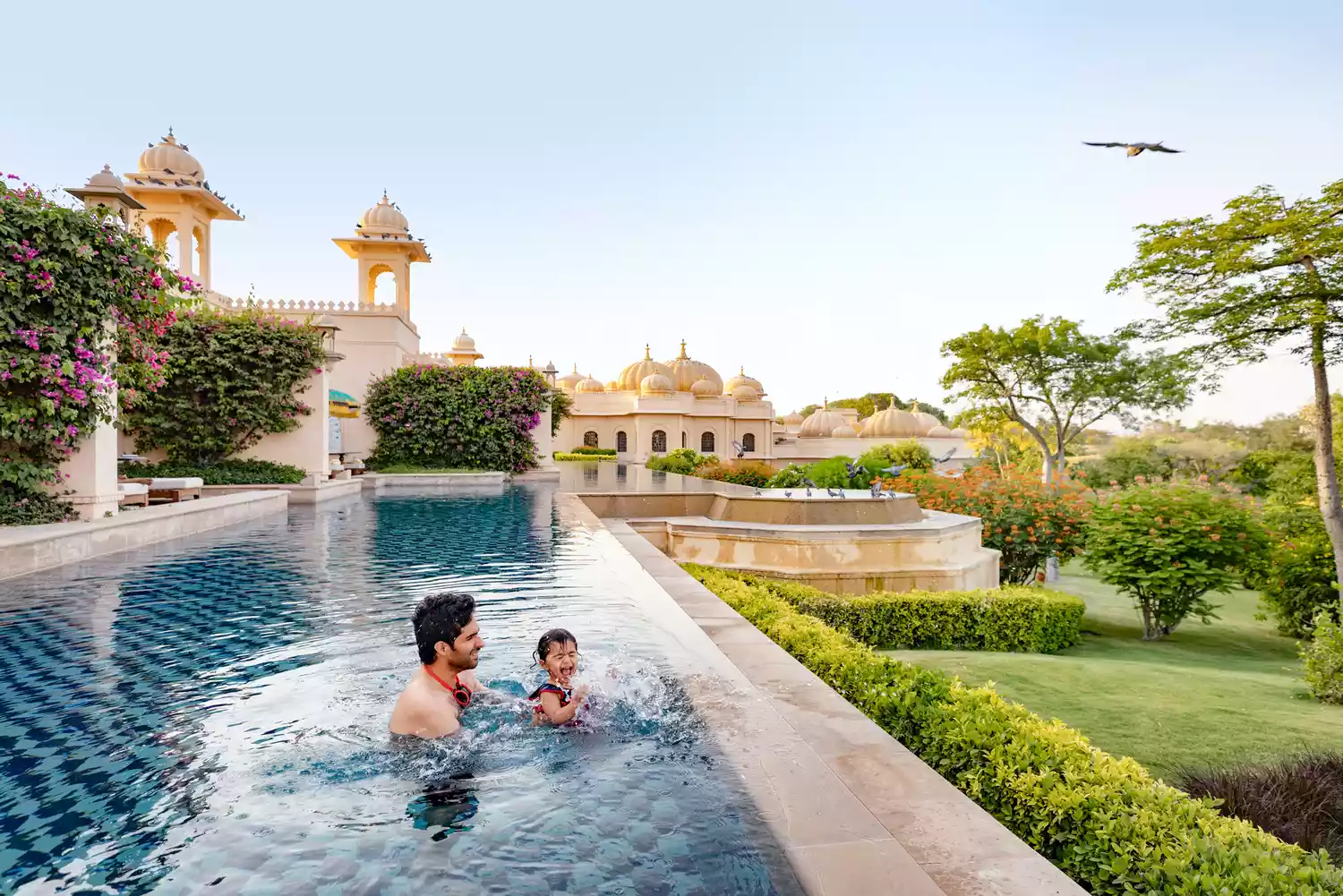 A father and young son playing and splashing in the clear blue water of a luxury resort swimming pool.