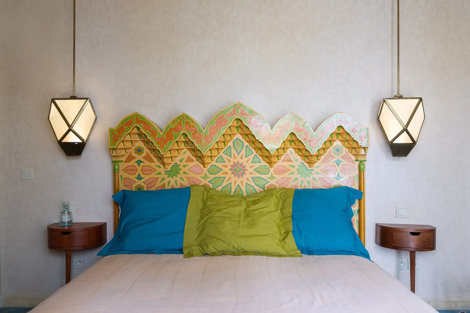 A luxury suite at Riad Romeo featuring a dark carved headboard and unique artistic hanging lights.