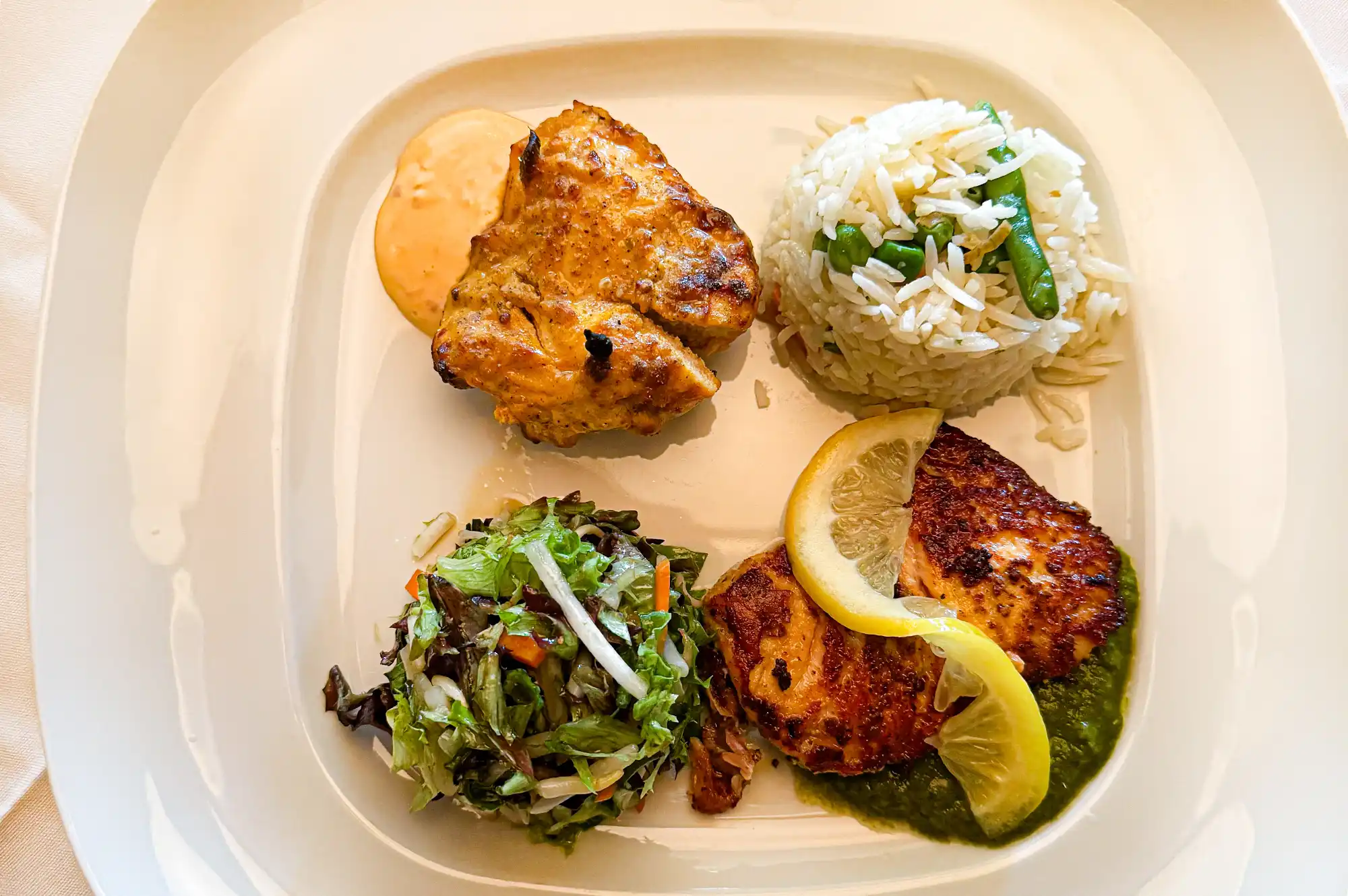An Indian lunch plate featuring grilled chicken, seasoned rice, salad, and garnished fish.