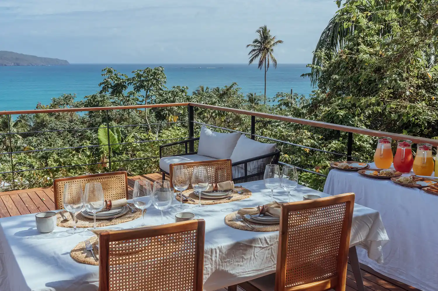 A set dining table on a private wooden terrace overlooking the ocean at sunset.