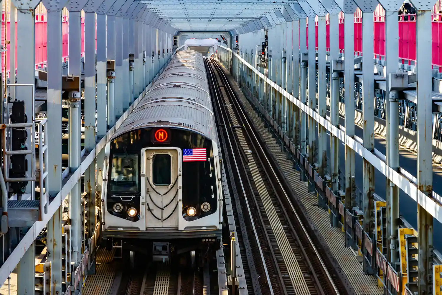 An NYC subway train traveling across the metal structures of the Williamsburg Bridge.