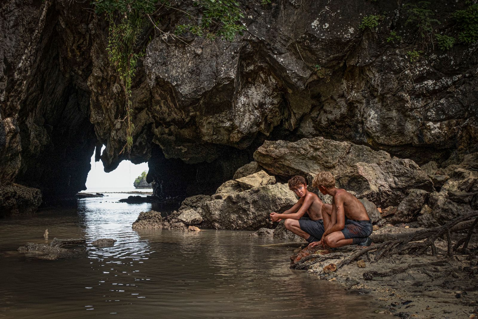 A young person sitting on a jagged rock formation by the edge of the sea.