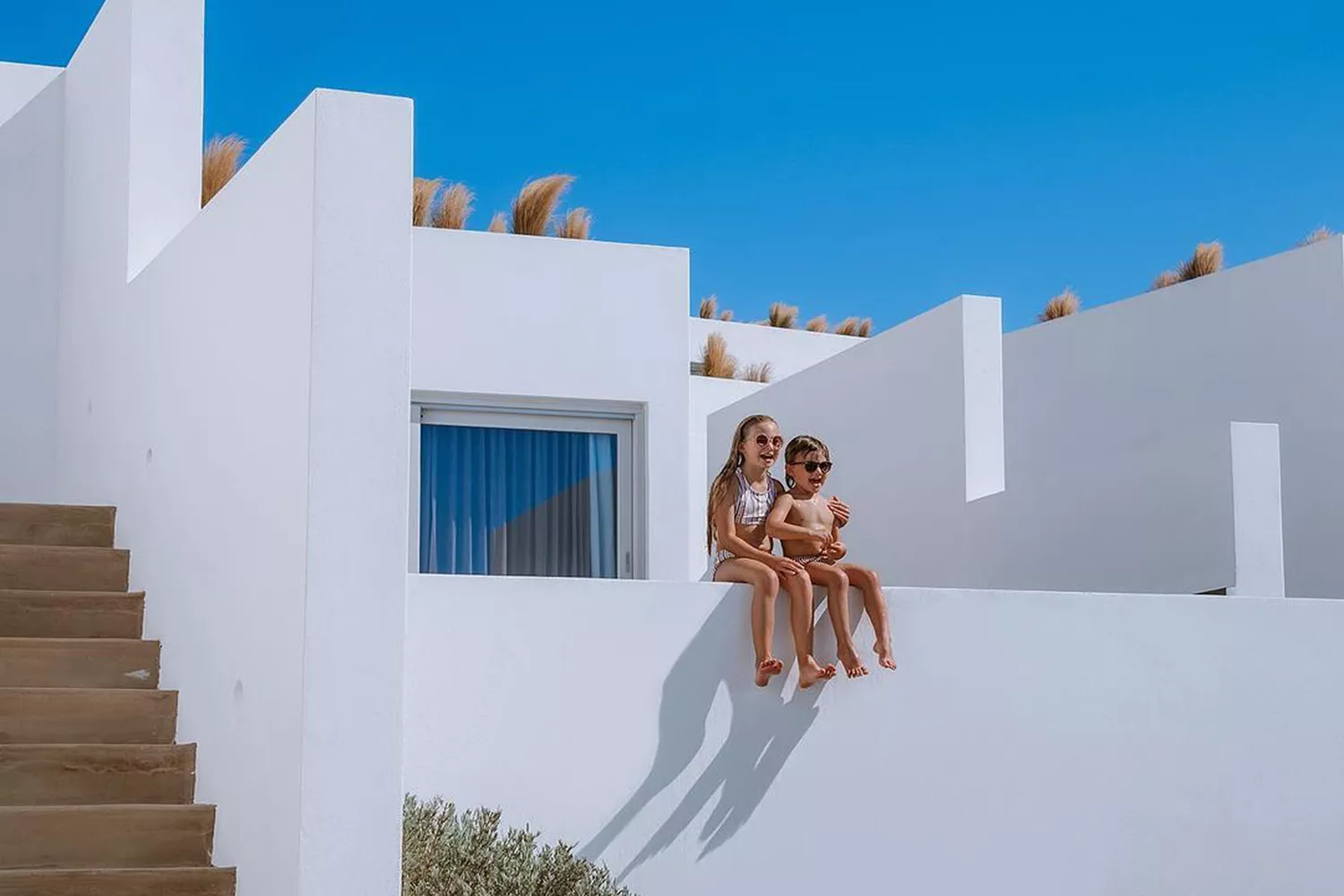 Children sitting on a stone wall at Andronis Arcadia, showing the resort's welcoming environment for families.